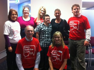 Eight people - four men and four women - standing some wearing red Every Australian Counts tshirts